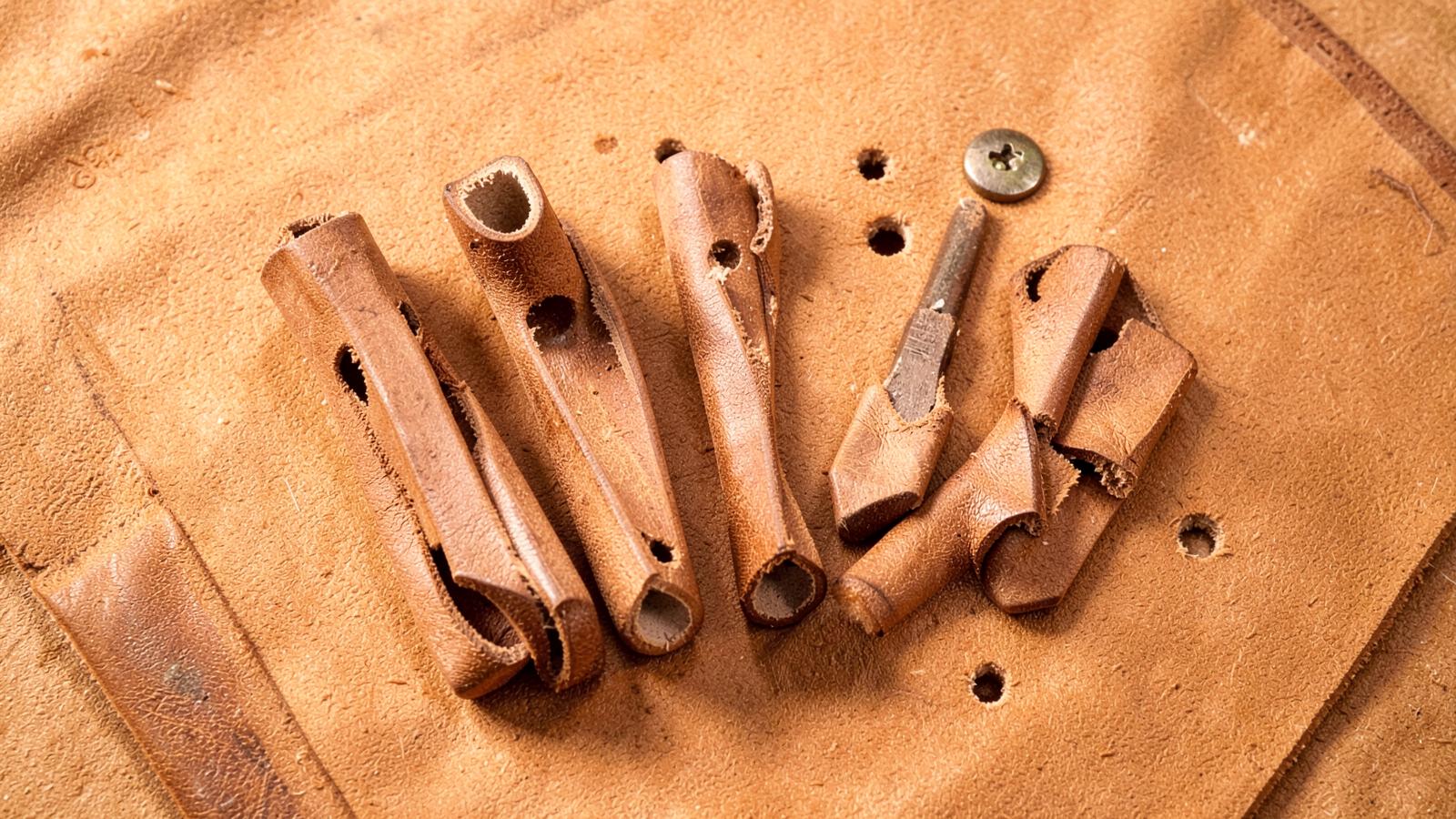Set of graduated hollow leather hole punches on tan leather with punched test holes and a rivet for scale.